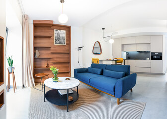 Panorama of a cozy stylish bright living room with natural ratan carpet, sofa, wooden shelf, plants, photos and modern lamps. Spacious modern studio interior in earthy colors a connected to the kitche