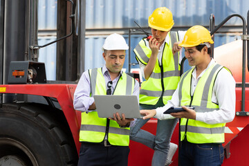 factory workers or engineers using laptop computer and talking about project work beside truck in containers warehouse storage