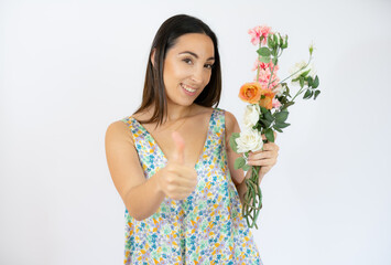 Beautiful woman holding bouquet of flowers with thumb up over white background