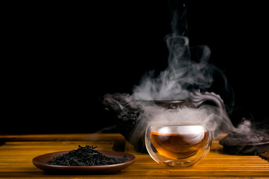 Chinese tea ceremony. Clay teapot with smoked red tea Lapsang souchong on a  black background, glass cups of hot tea with vapour. Stock Photo