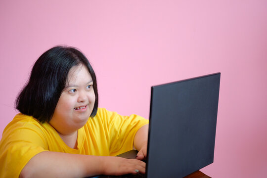 Portrait Of A Mentally Disabled Young Woman Called Down Syndrome Children Working And Learning With Laptop Pink Background