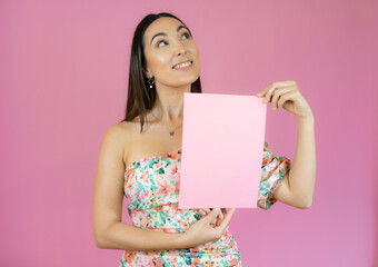 Young beautiful woman smiling and holding a blank sheet of paper isolated over pink background.