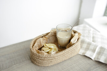 Handmade home decor. oval jute basket with wooden bottom, tray, food stand, table setting. the concept of home decor and comfort in the eco style. a rice cake with a banana and a clear glass of latte.
