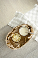 Handmade home decor. oval jute basket with wooden bottom, tray, food stand, table setting. the concept of home decor and comfort in the eco style. a rice cake with a banana and a clear glass of latte.