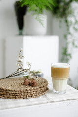 Obraz na płótnie Canvas Handmade home decor. round jute napkins, hot plate, table setting. the concept of long-term decor and comfort in the eco style. chocolate candy truffle. A clear glass of latte coffee. Checkered linen 