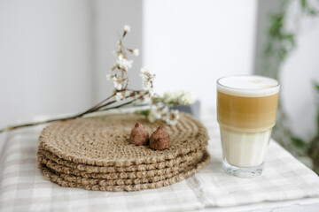 Handmade home decor. round jute napkins, hot plate, table setting. the concept of long-term decor and comfort in the eco style. chocolate candy truffle. A clear glass of latte coffee. Checkered linen 