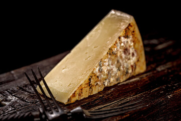 Close-up of a piece of cheddar cheese. Aged cheese made from farm milk, an old English recipe. A piece of cheese on a dark wooden board and a cheese knife. Low key image.