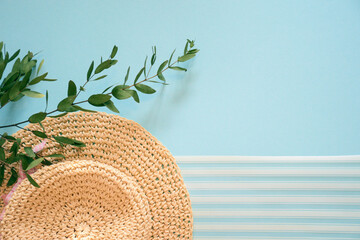 Straw hat and a branch of myrtle on a blue background with white stripes. Vacation & travel concept, top view, flat lay, beach hat and green myrtle with copy space.