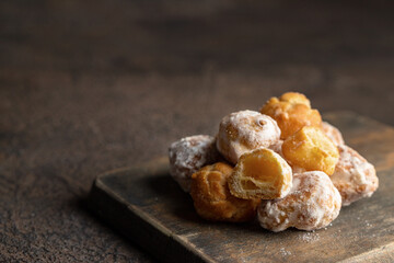 Buttery little pastries, Profiteroles dusting with powered sugar  on wooden board in dark mood background..