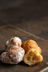 Buttery little pastries, Profiteroles dusting with powered sugar  on wooden board in dark mood background..