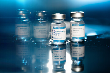 Two Covid-19 vaccine vials reflected on blue and black background
