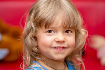 Portrait of a small laughing girl with blonde hair in a room on a colored blurred background, close-up, selective focus.