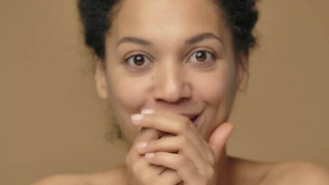 Beauty portrait young African American woman looking at camera with excitement, delight and wow facial expression. Black female on brown studio background. Close up. Slow motion ready, 4K at 59.94fps.