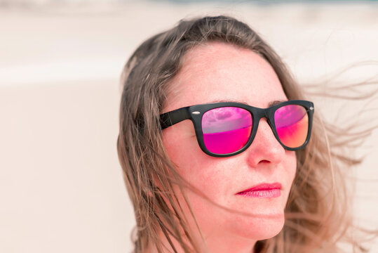 Beautiful young woman in sunglasses is looking to the sky in a windy day on the white sand beach.