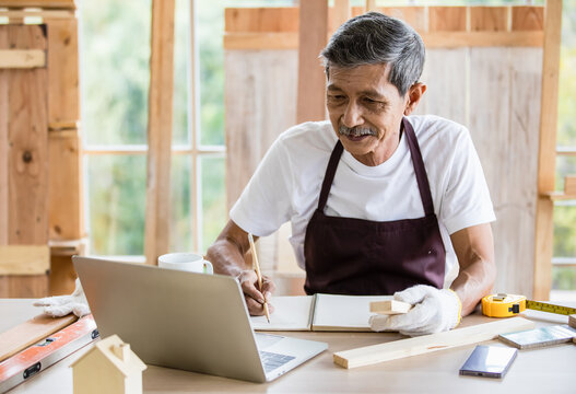 Senior Asian carpenter writing down data from laptop