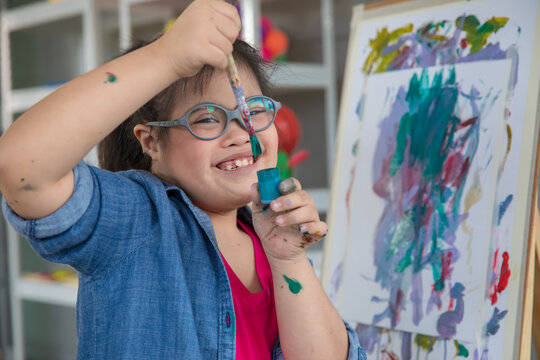 Happy girl with Down syndrome painting on easel