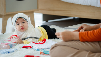 A cute and beautiful Asian Muslim mother selects and arrange clothes for her baby daughter while...
