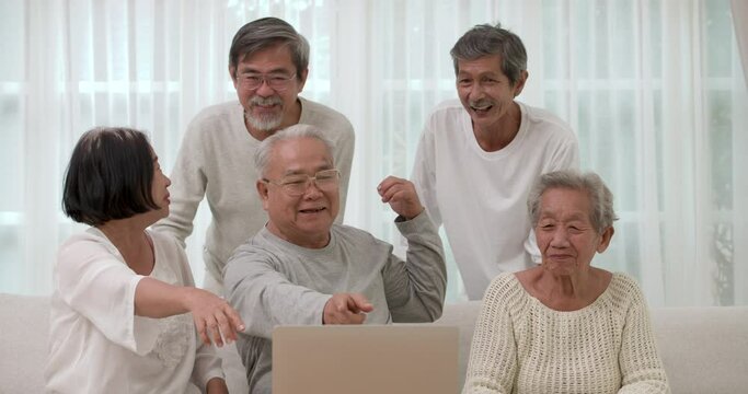 A Group of happy Asian seniors male and female using laptop for video call or facetime with their old friends in living room. The old man and woman sitting together and having a facetime on computer.