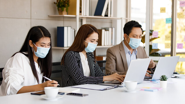 coronavirus prevention in the office. Group of Asian businesspeople wearing face masks and wearing formal clothes working at the office table. Covid-19 new normal lifestyle concept