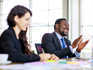 Portrait of a happy handsome African businessman clapping a hand in a multiracial meeting at the conference room with cute smiling with businesswoman foreground. Concept of happiness business work