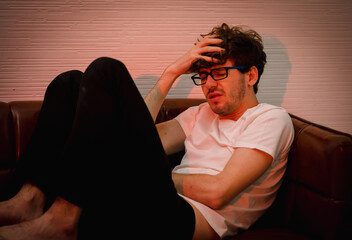stressful caucasian man dressed casually sitting on a couch leaning against backrest hand holding...