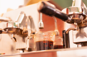 Grinder machine makes black coffee and flows it into coffee measuring cup at coffee bar. Barista work at coffee counter bar in cafe coffee shop for food and coffee service business