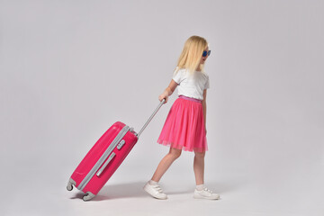 Teenage girl rolling pink suitcase on gray background with copy space