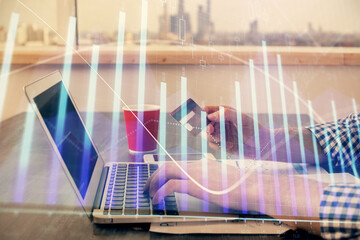Double exposure of man hands holding a credit card and Forex graph drawing. Stock trading and digital fintech in Internet E-commerce concept.