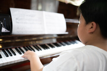 A boy is studying piano online with tablet.