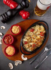 Baked champignons mushrooms, with cheese, parsley and roasted garlic in black bowl.