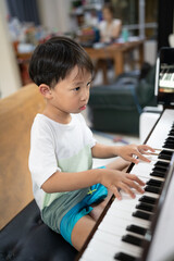 A boy is studying piano online with tablet.