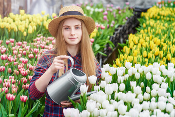 Happy smiling teenager girl in hat with watering can in blossoming tulip garden