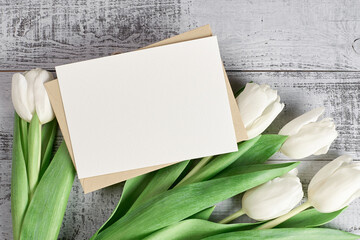 Greeting card mockup with white tulip flowers and envelope on rustic wooden background