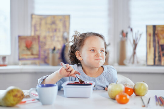 Funny laughing girl is having dinner sitting at the table stuffed mouth with food. Small cute schoolgirl having lunch. Eating using fork from lunch box. Tasty eating concept. High quality image