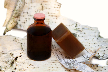 Liquid tar in a bottle and tar soap on birch bark background