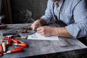Beautiful bearded brunette craftsman in apron and eyeglasses making sketch using felt pen. Linocut professional artist handmade worker. High quality photo
