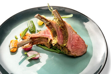 Crusted lamb ribs cutlets with bone in green dish with carrot, radishes and courgette, close up