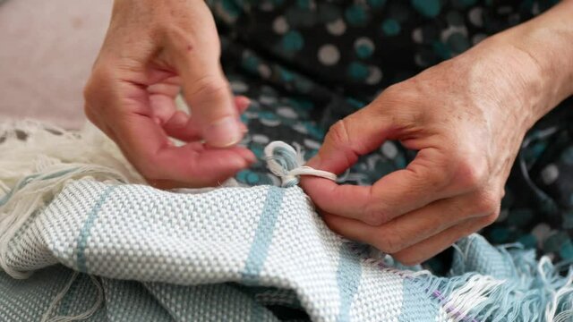 Creating a fringe on a woven shawl. Hands of artisan at work, close up