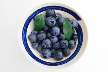 Blueberries in a white cup on a white background.  Close-up view of fresh Blueberries top view. Collection of blue and black berries. Conceptual food image. Concept of healthy food and diet.