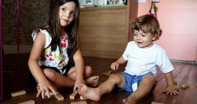 Baby brother kicking sister building wooden blocks play