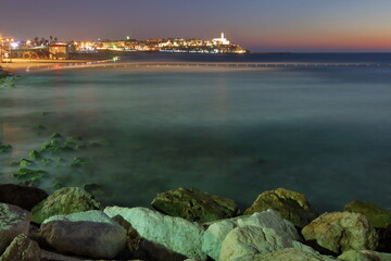 sunset over the sea, rocky shore in Tel Aviv, Israel, on horizon evening lights of Jaffa