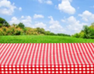 Empty table with red and white tablecloth over blurred park nature background, for product display montage, spring and summer