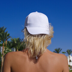 white baseball cap mockup, young beautiful girl with blonde hair in a white baseball cap on a background of blue sky and palm trees.