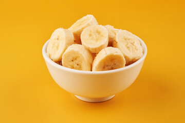 White cup with sliced bananas on a yellow background. Tropical fruits, healthy food, vitamins