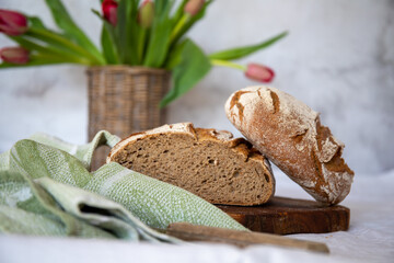 Sliced rye bread on cutting board close-up and a wicker vase with tulips in the background