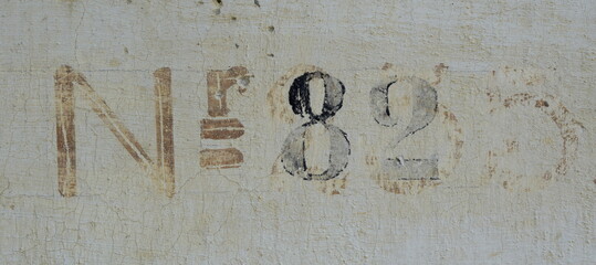 Hausnummer 82 auf einer alten Hausmauer mit Farbe aufgetragen in alter Schrift - braun, beige und schwarz