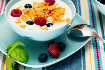 Breakfast of cornflakes and raspberries, blueberries and milk in a blue plate