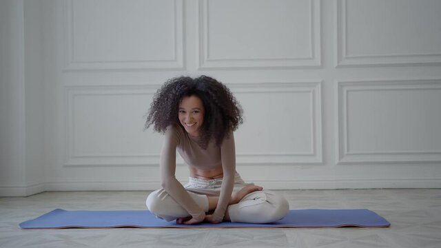 Young african woman on a blue sports mat in white living room, hard to do sport exercises. Non-athletic, unsporting beautiful woman falling while doing exercises