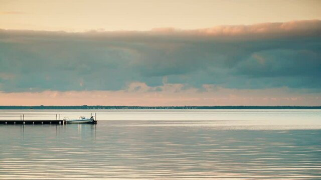 Seascape at evening with boat tied to wooden pier. Baltic Sea, Puck Bay in Poland with Hel Peninsula on horizon. Seaside coast landscape.