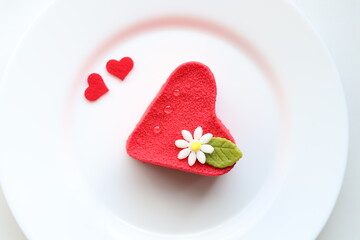 Top view of heart shaped cake with a flower on top on white plate decorated with two small hearts